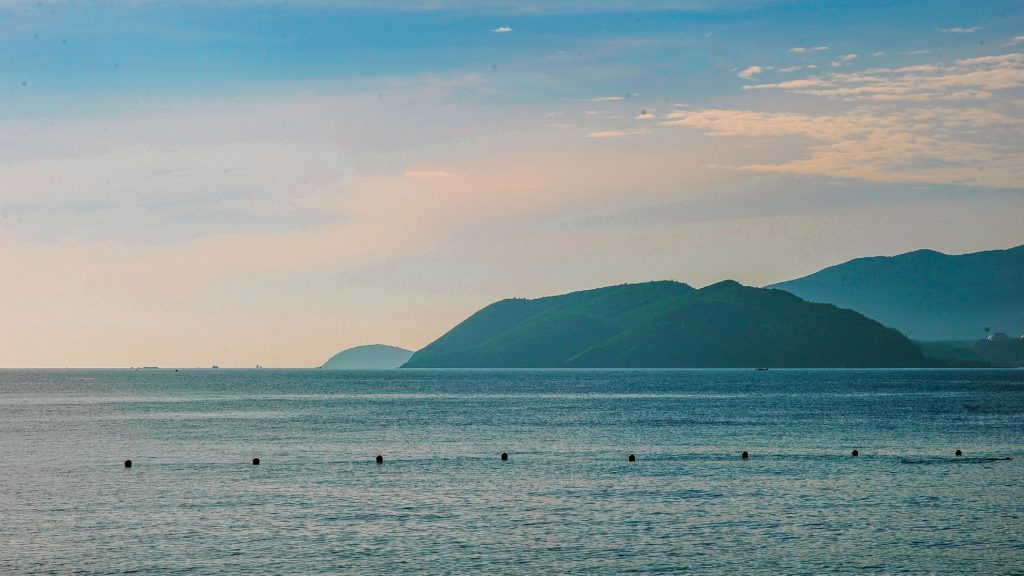 Peaceful ocean scene with distant mountains under a clear sky at dawn.